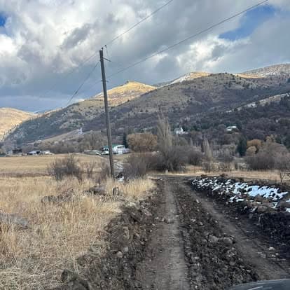 Rugged dirt road winding through hilly landscape with scattered houses and cloudy sky.