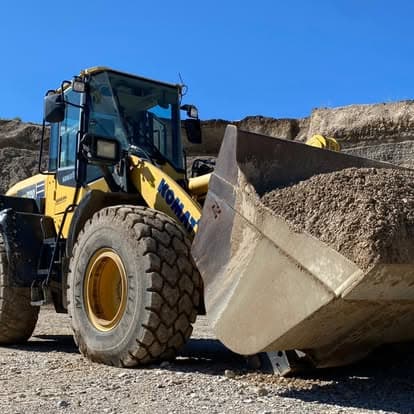 Kobelco construction loader with a bucket of gravel on a worksite under clear blue skies.