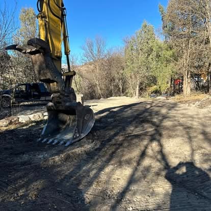 Excavator bucket on dirt road with trees and blue sky in background. Construction scene.