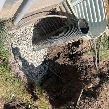Drainage pipe installation in a gravel-filled trench, with surrounding soil removed.