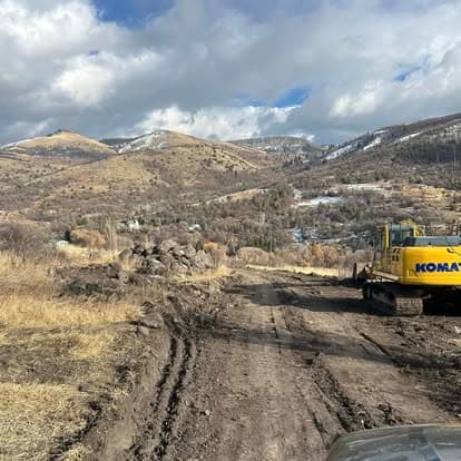Construction vehicle on a dirt road in mountainous terrain, with rocky landscape and cloudy sky.
