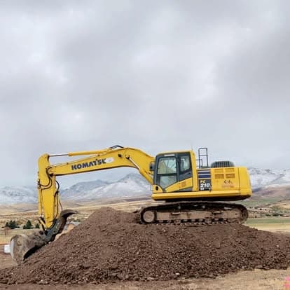 Komatsu excavator on a dirt pile with mountains in the background under a cloudy sky.