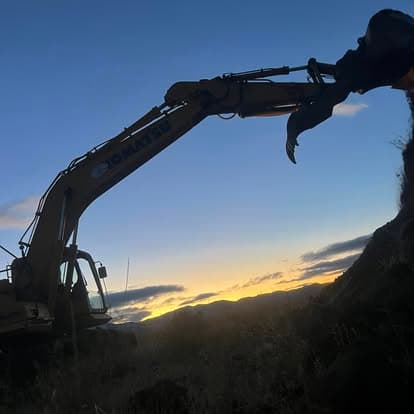 Excavator silhouetted against a sunset sky in a rural landscape.
