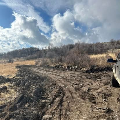 Off-road vehicle on a rugged dirt path with cloudy skies and hills in the background.
