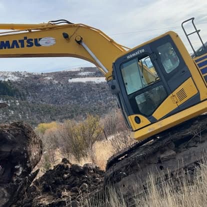 Komatsu excavator on steep terrain with a mountainous backdrop. Heavy machinery in action.