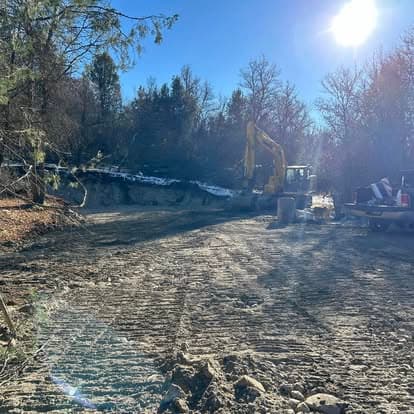 Excavator working on a construction site surrounded by trees and clear blue sky.