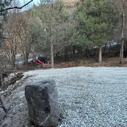 Excavated area with gravel and red construction equipment among trees in forested landscape.